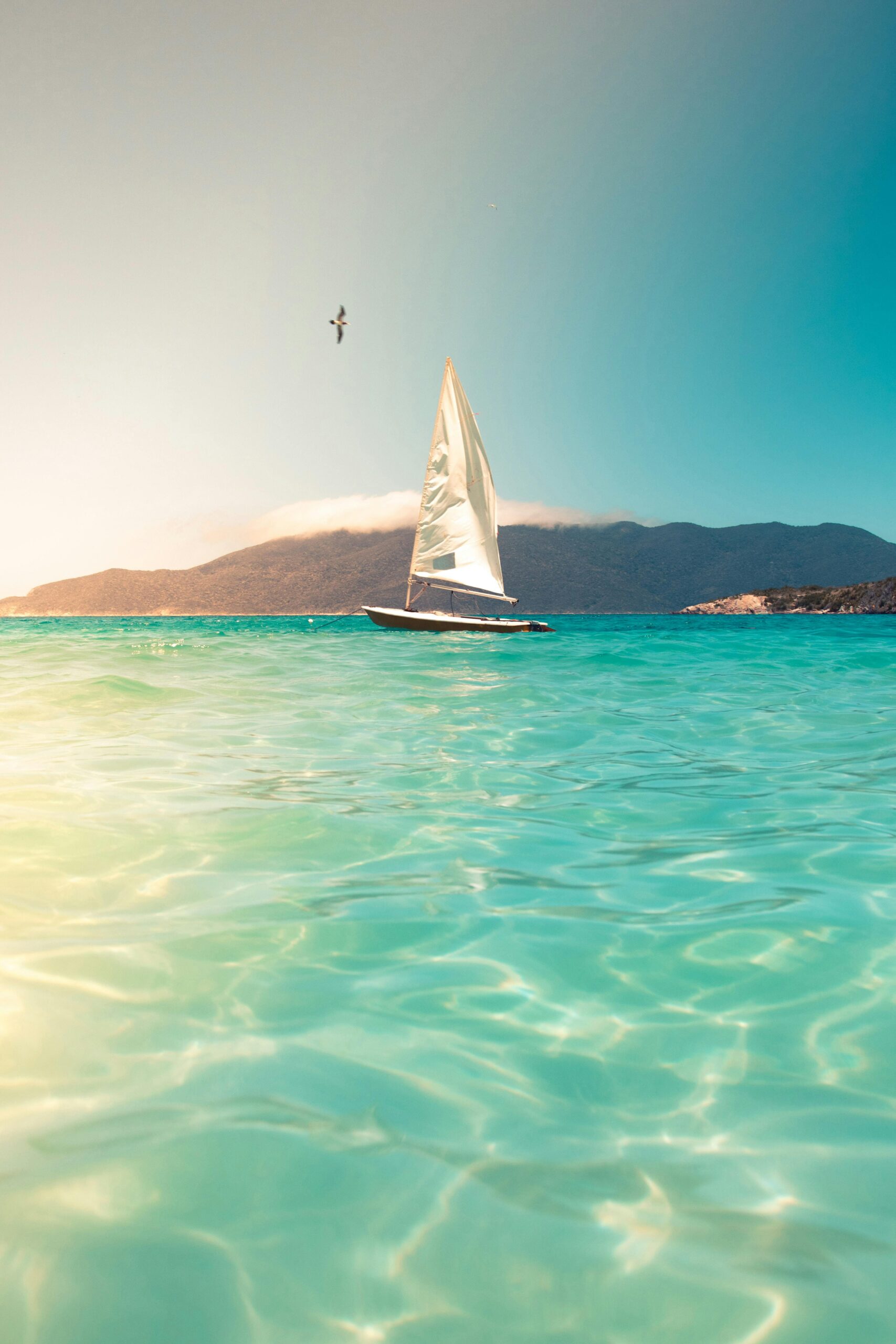 A sailboat glides across turquoise seas beneath a clear sky, ideal for tranquil travel and vacation scenes.